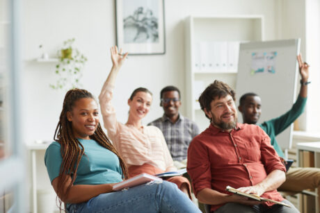 Multi-ethnic group of people raising hands while answering questions during training seminar or business conference in office