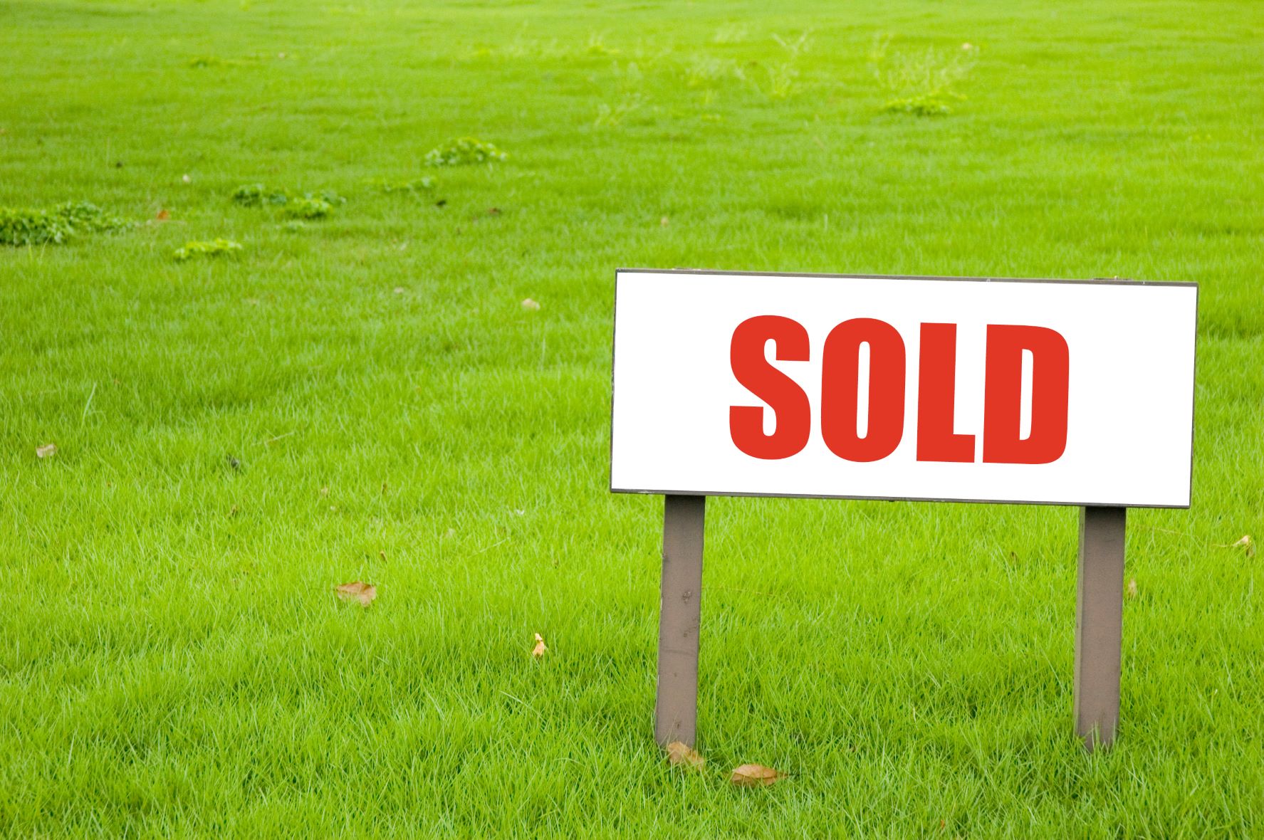 Photo of a grassy field with a "Sold" sign on it.