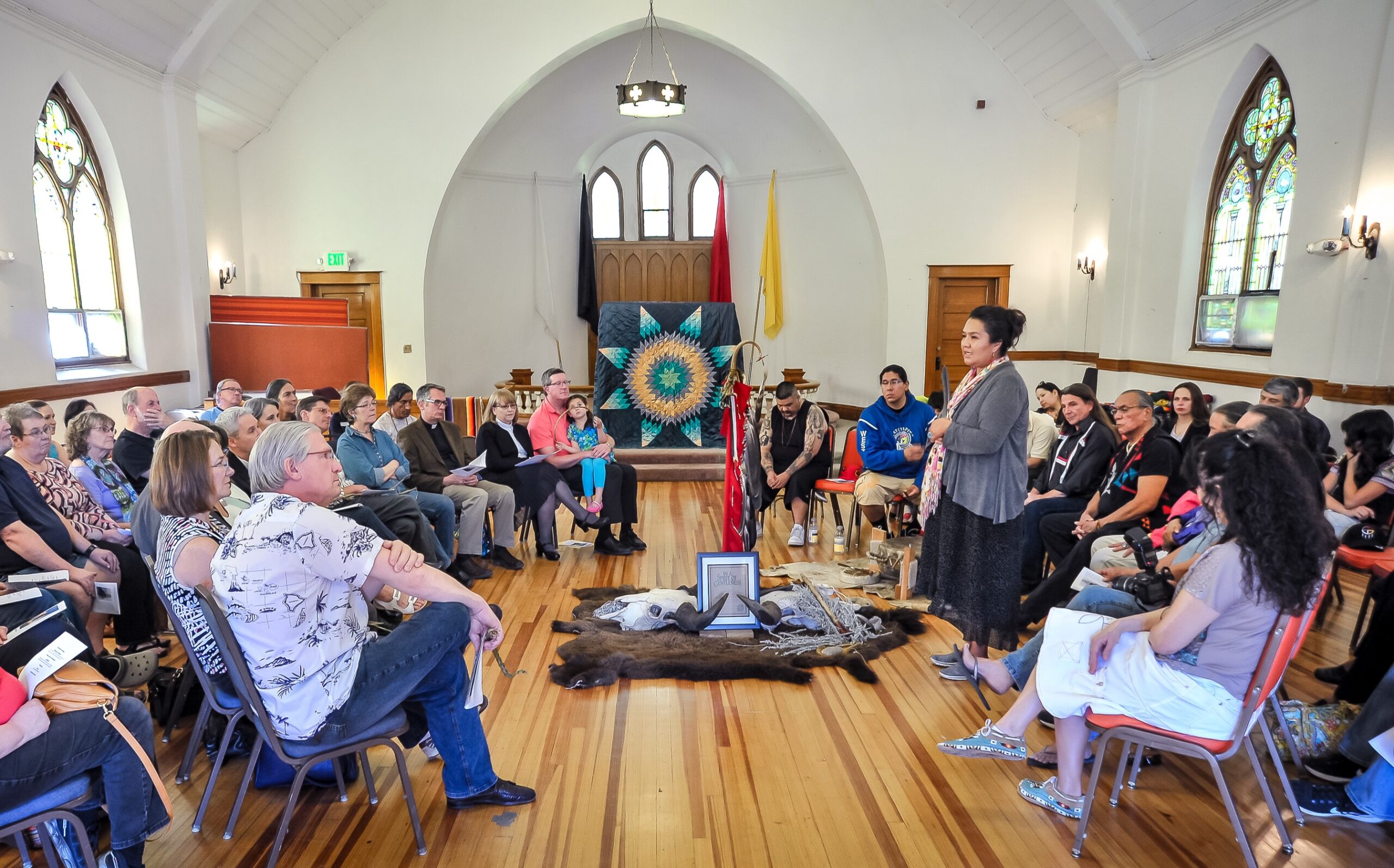 People sit in a circle around object of significance in a church building, with one person speaking in the center.