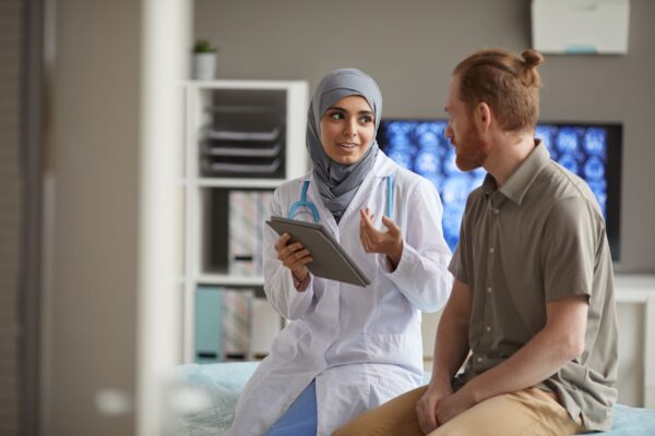 A female doctor wearing a hijab explains something to a male patient in a health clinic