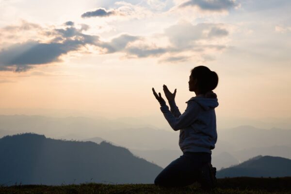 silhouette of a person kneeling with hands raised on top of a mountain