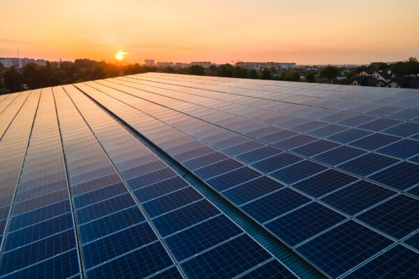 Photo of an urban roof with solar panels as the sun sets in the background.