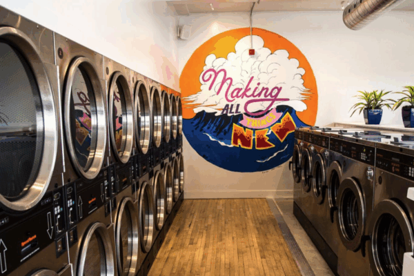 Photo of laundry machines with plants on top and a wall mural that reads: Making All Things New