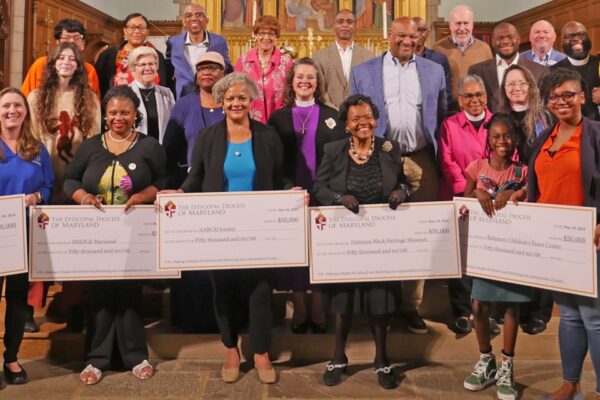 Photo of a group of people standing at the front of a church, the five people in front hold symbolic donation checks.
