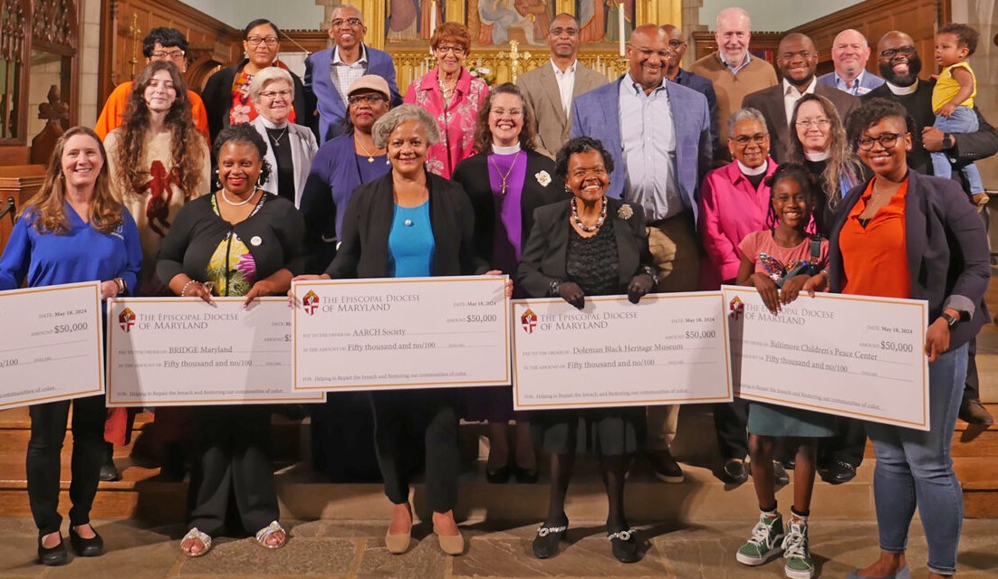 Photo of a group of people standing at the front of a church, the five people in front hold symbolic donation checks.