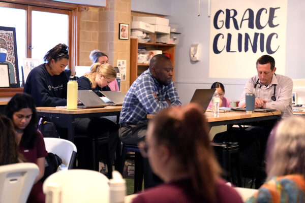 Photo of people in scrubs, with stethoscopes, and regular clothing closing their eyes while they sit in a repurposed church sunday school room.