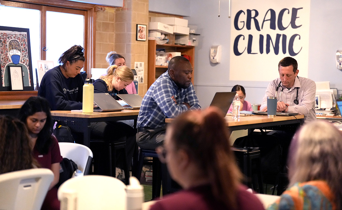 Photo of people in scrubs, with stethoscopes, and regular clothing closing their eyes while they sit in a repurposed church sunday school room.