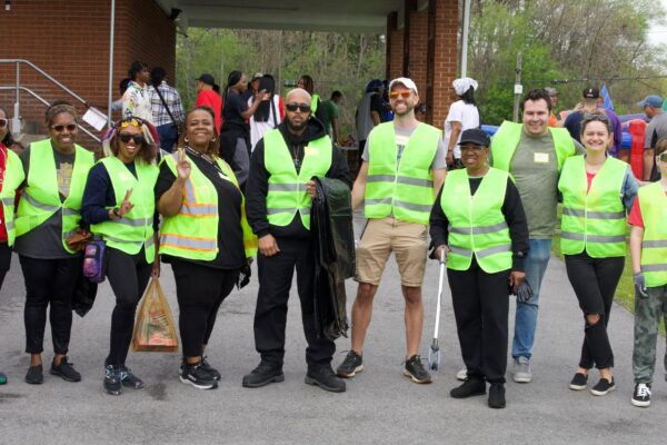 A group of people wearing safety vests and holding trash pickup tools to pose for a photo together, smiling.