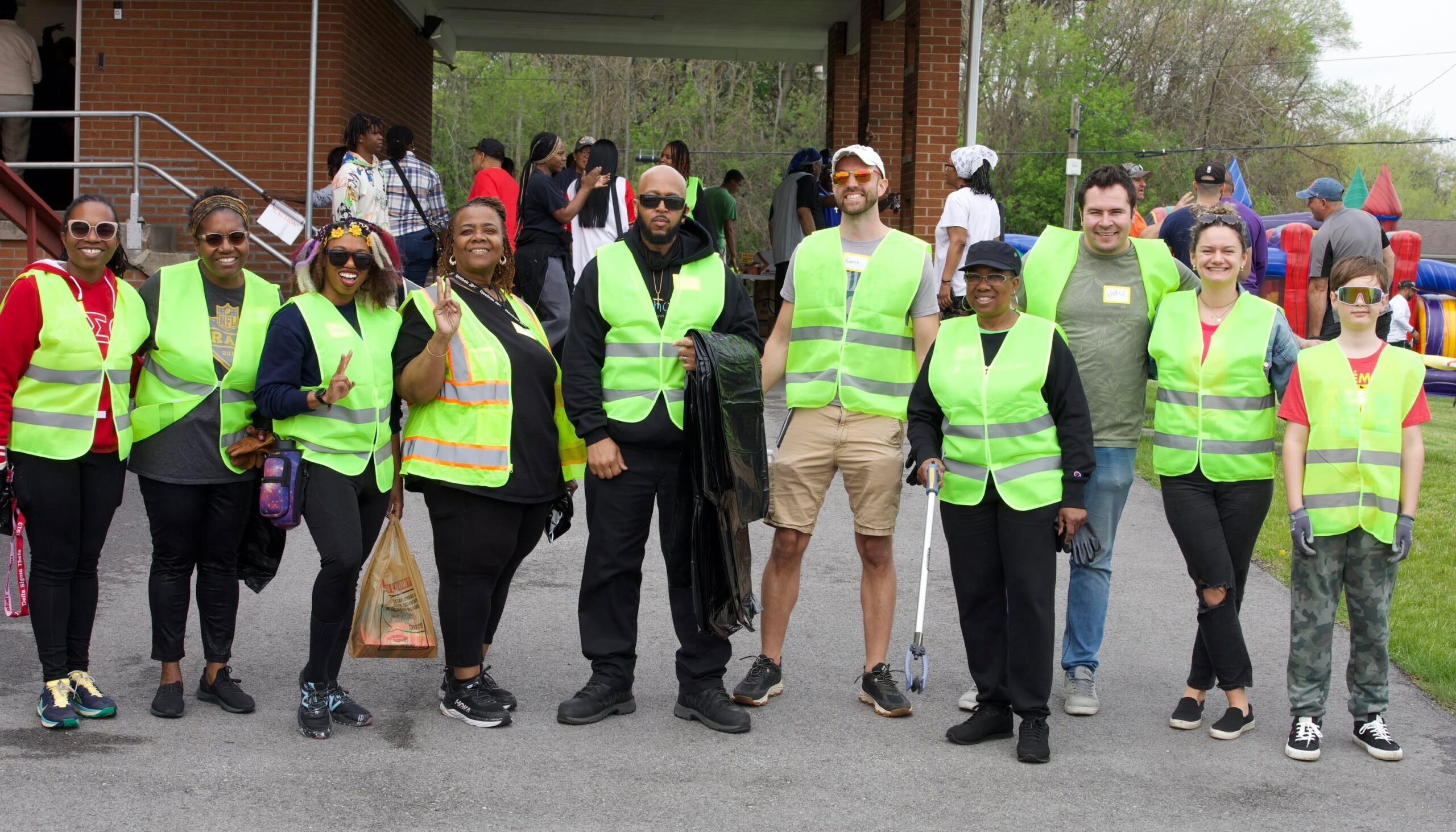 A group of people wearing safety vests and holding trash pickup tools to pose for a photo together, smiling.