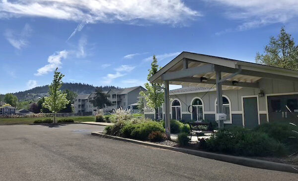 Exterior view of a small covered pavilion and office building with arched windows, in a residential neighborhood, with forested hills and blue sky in the background